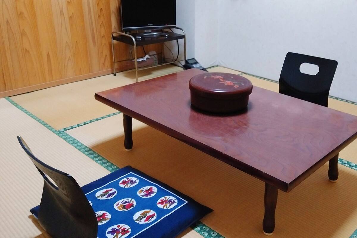 Una stanza con tatami, un tavolino in legno basso, un cuscino e una sedia.