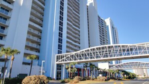 A modern high-rise hotel with multiple balconies, a pedestrian bridge, and palm trees. - 5 Pools, 2 heated indoor. 3 hot tubs, movie theater, Starbucks and bar and grill (Panama City Beach)