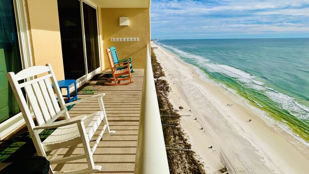 A balcony with a view of a beach, featuring a white rocking chair, a blue chair, and a small table. - 5 Pools, 2 heated indoor. 3 hot tubs, movie theater, Starbucks and bar and grill (Panama City Beach)