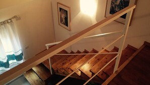 Uma escada de madeira com corrimão, uma janela com cortinas e duas molduras com quadros na parede.