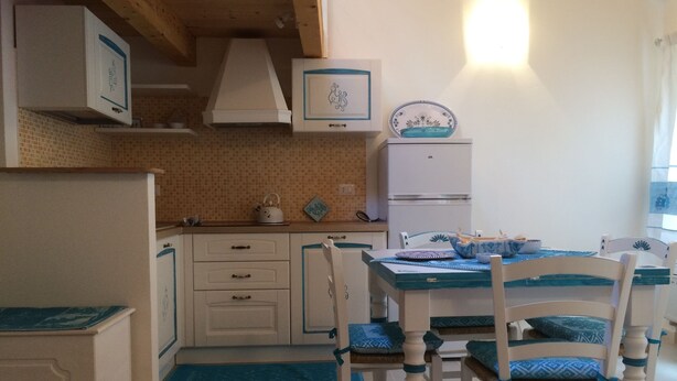 Cozinha com armários brancos, painel de azulejos, geladeira branca e mesa azul e branca com cadeiras.