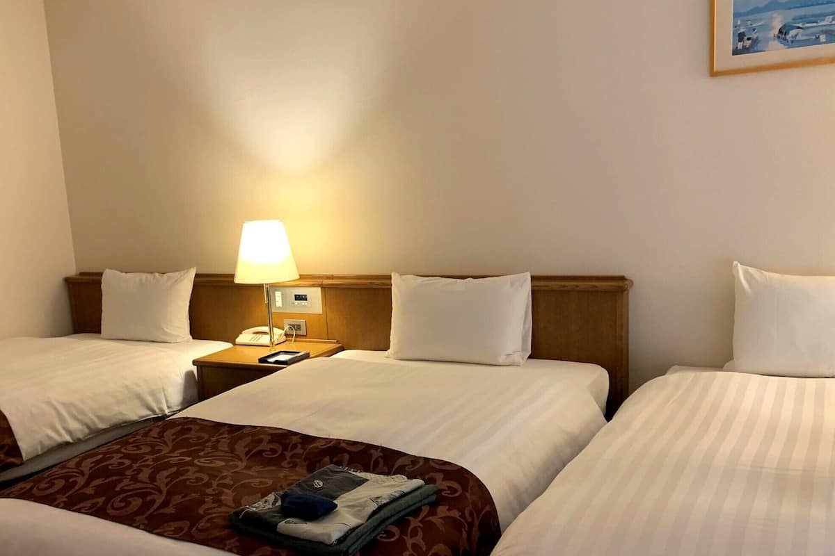 A hotel room with two beds, a bedside table with a lamp, a phone, and a painting on the wall.