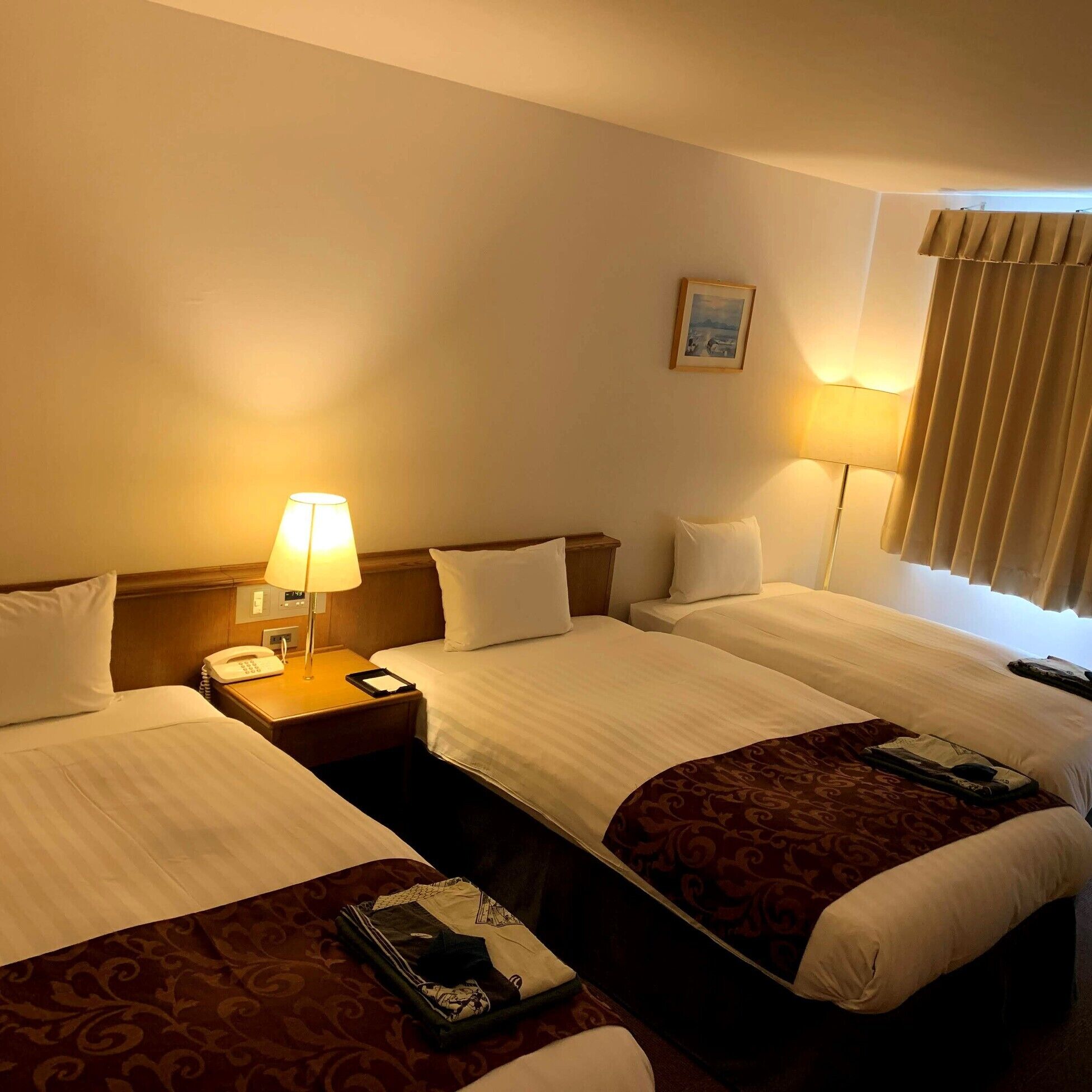 Ein Hotelzimmer mit zwei Betten, einem Nachttisch mit Lampe, einem Telefon und einem Bild an der Wand.