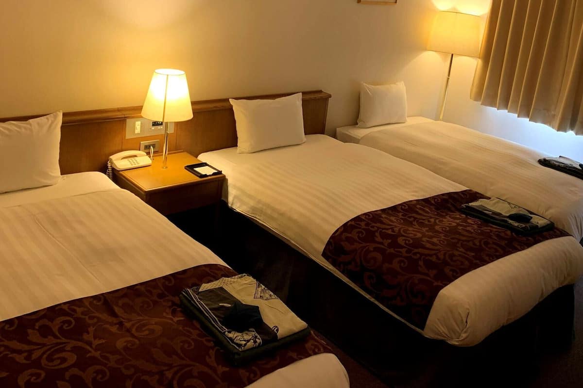 A hotel room with two beds, a bedside table with a lamp, a phone, and a picture on the wall.