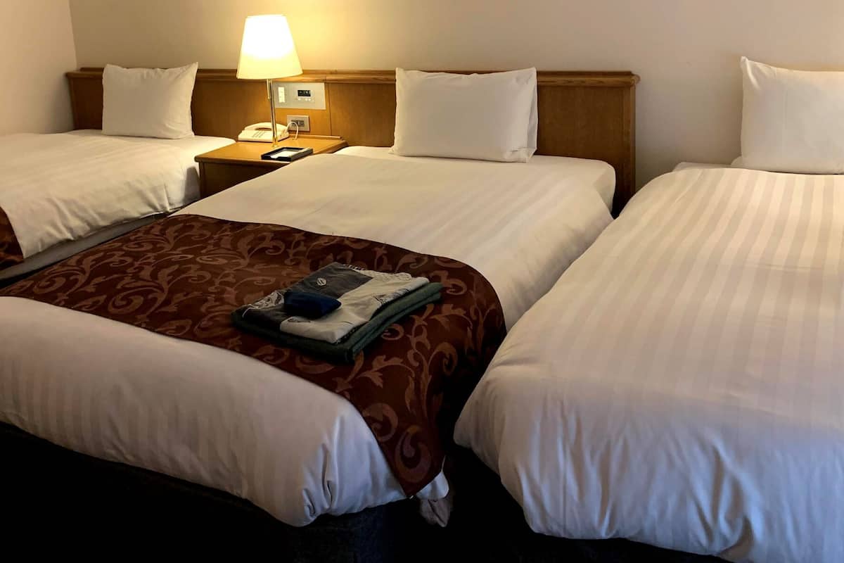 A hotel room with two beds, a nightstand with a lamp, a phone, and a painting on the wall.