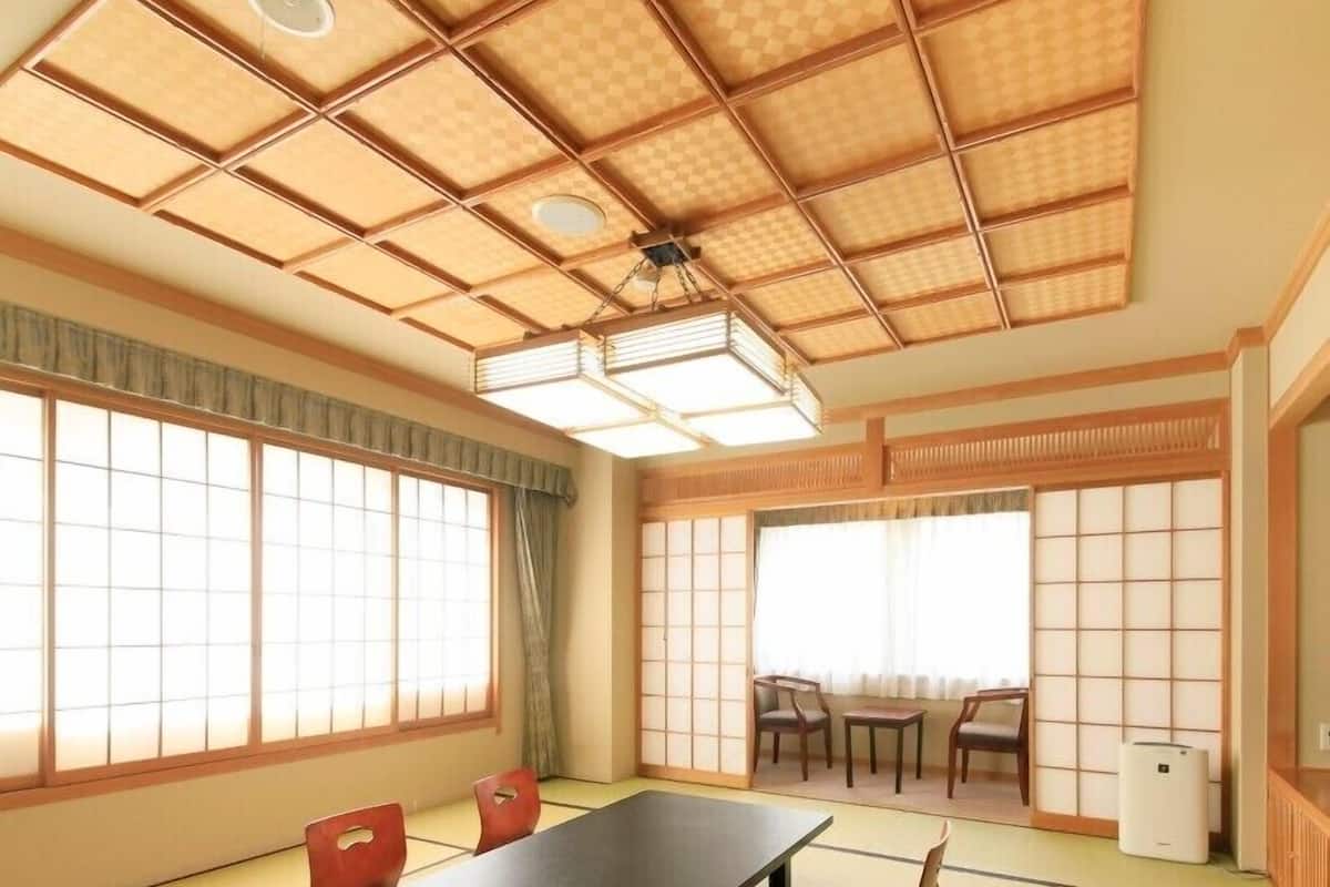 A tatami mat room with a low table and chairs, large windows, and a ceiling fan.