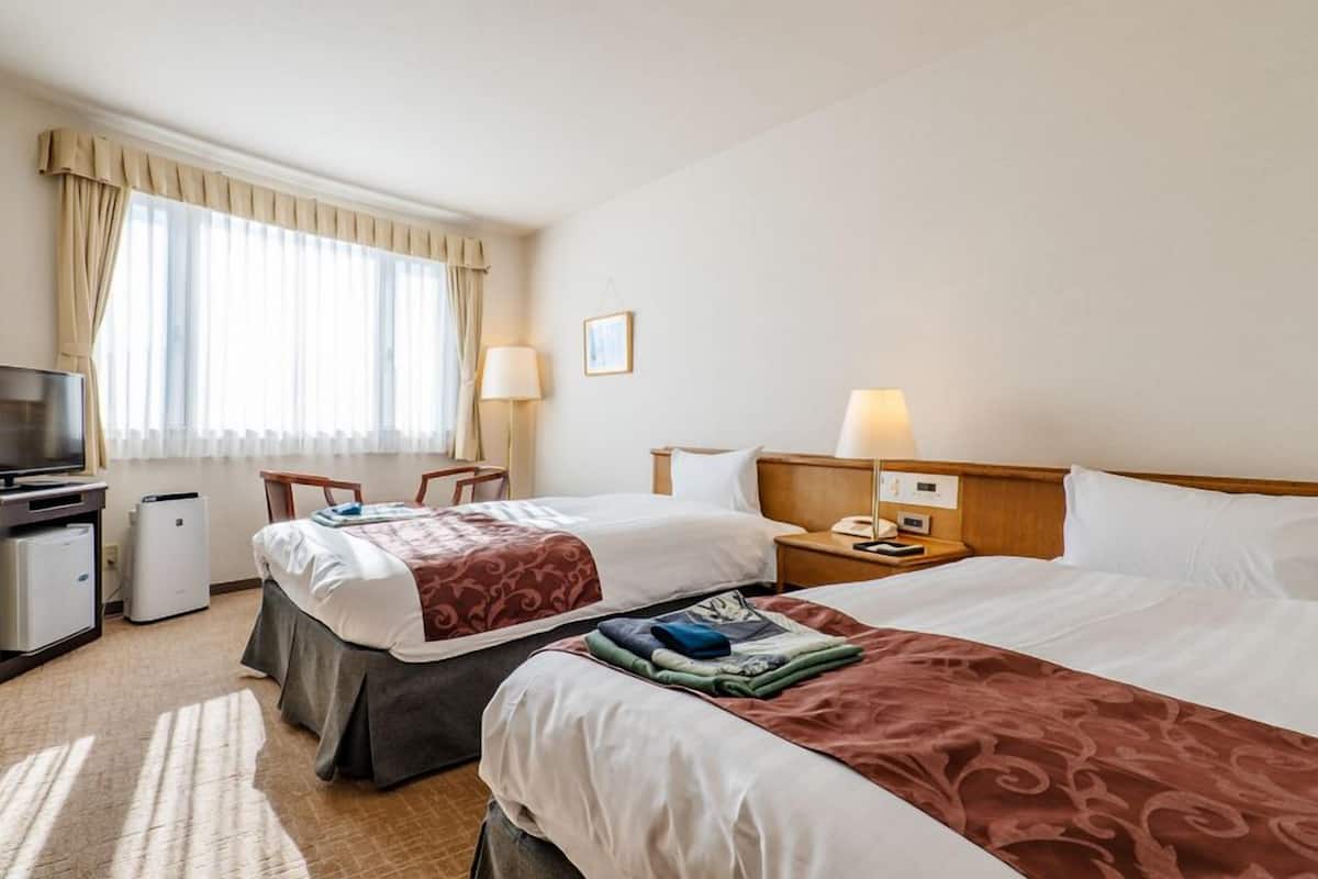 A hotel room with two beds, a desk with a computer, a TV, and a window with curtains.