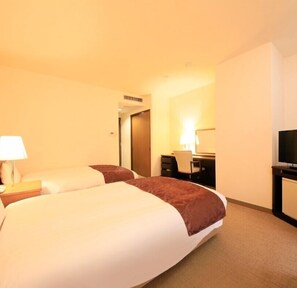 A hotel room with a large bed, a desk, a chair, a TV, and a lamp.