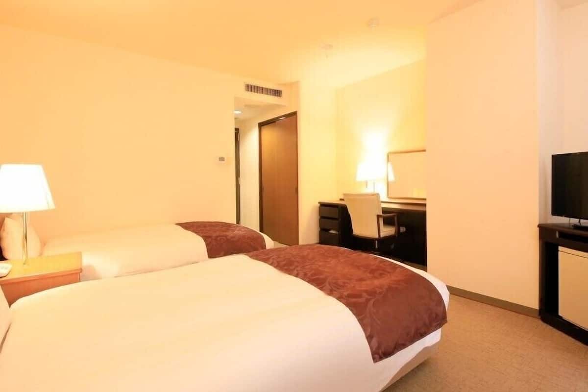 A hotel room with a large bed, a desk, a chair, a TV, and a lamp.