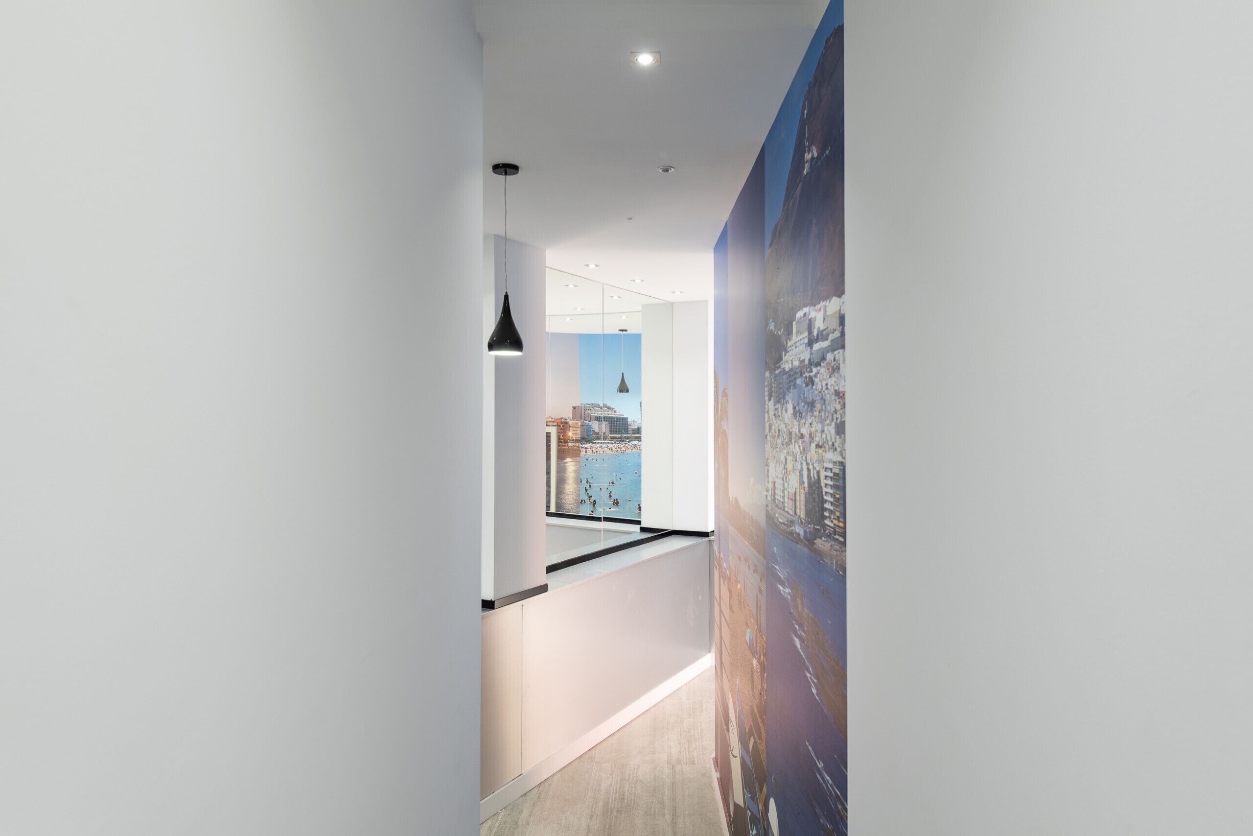 Een moderne hal met uitzicht op een stadsbeeld door een raam, een hanglamp en een groot poster aan de muur.