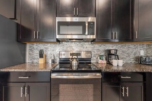 Una cocina moderna con armarios oscuros, un microondas de acero inoxidable, una tetera y una cafetera.