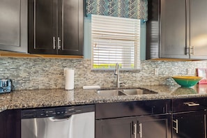A kitchen with dark cabinets, a granite countertop, a stainless steel sink, and a patterned backsplash.
