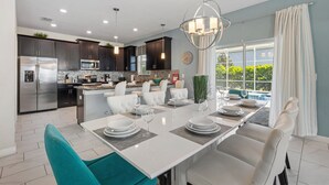 Une cuisine moderne avec des meubles de couleur sombre, des appareils en acier inoxydable et un coin repas agrémenté d’une table blanche dressée pour six personnes.
