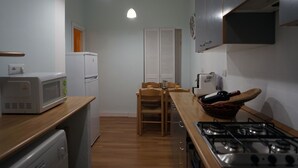 A compact kitchen with a microwave, refrigerator, stove, and wooden dining table. - Casa Cappone (Alghero)