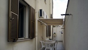 A narrow alleyway with a white table and chairs under a canopy, flanked by buildings with shutters and air conditioning units. - Casa Cappone (Alghero)