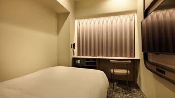 Una camera d'albergo con un letto, una scrivania con una sedia, una televisione e una finestra con tende.