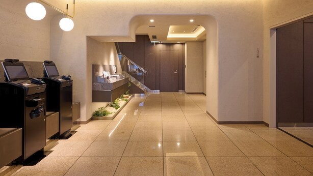 Un hall d’hôtel moderne avec un comptoir d’accueil, un escalier et un sol carrelé impeccable.