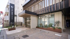 Un bâtiment moderne doté d’une entrée imposante, d’une enseigne indiquant « VIA INN SHINJUKU » et d’un espace paysager agrémenté de jardinières.