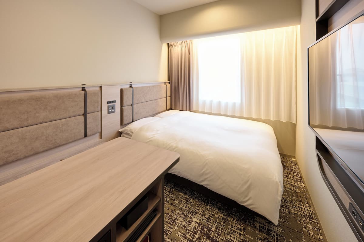 A hotel room with a bed, a desk, a TV, and a window with curtains.