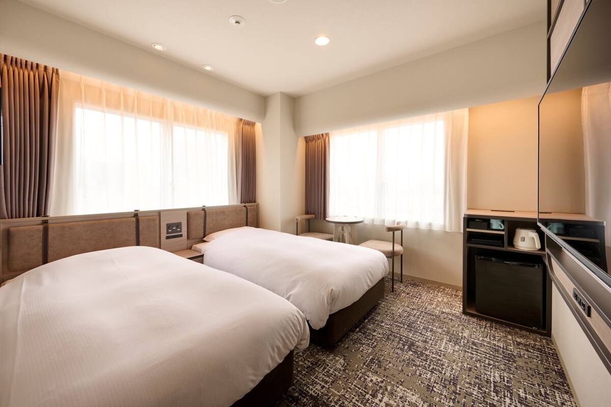 A hotel room with two beds, a small table, a TV, and a coffee maker.