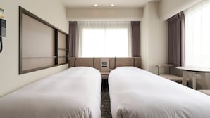Une chambre d’hôtel avec deux lits simples, un petit canapé, une table ronde et une fenêtre avec des rideaux.