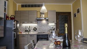 A modern kitchen with a dining table set for two, a wine bottle, and glasses. - Casa Barracuda (Alghero)