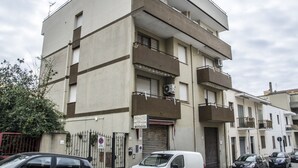 A multi-story building with balconies, a closed garage door, and a sign indicating a motor office. - Casa Barracuda (Alghero)