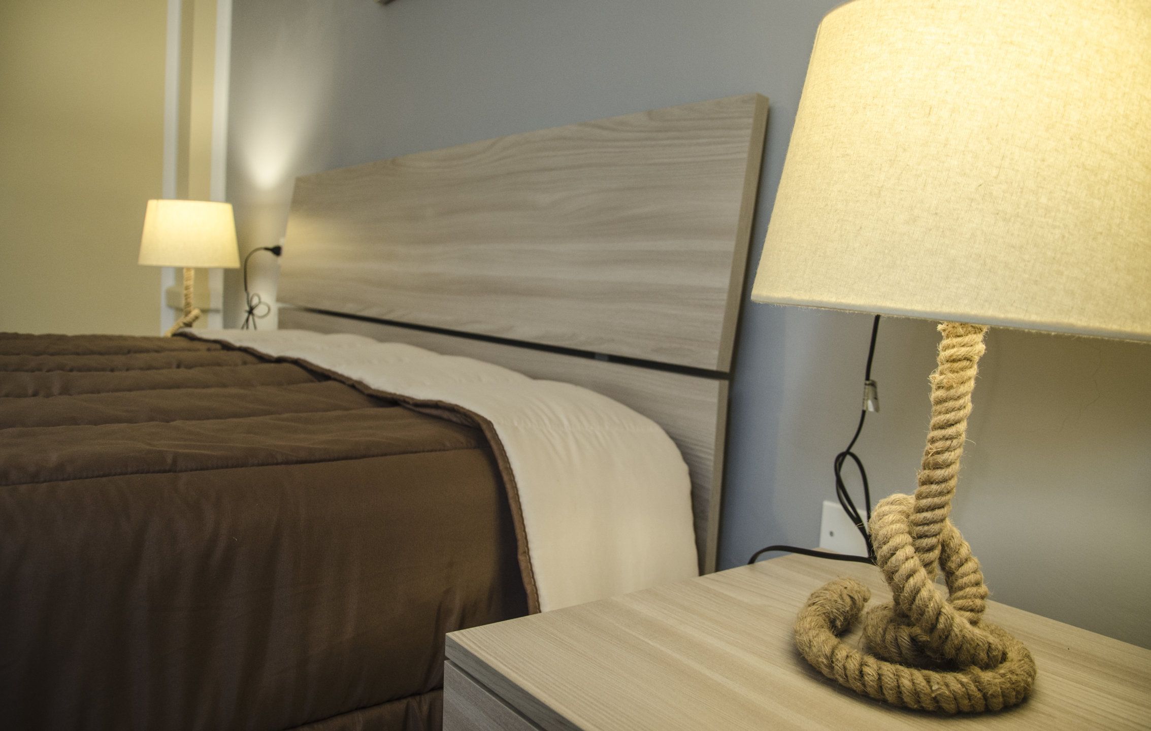 Un lit bien fait, avec une couette marron, une tête de lit en bois et une lampe de chevet dont le pied est en corde.