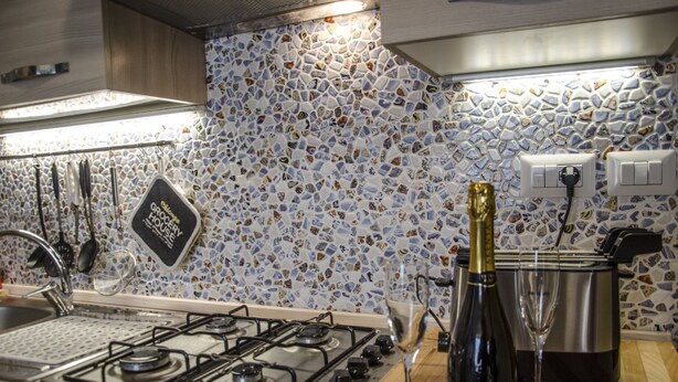 A kitchen with a gas stove, a wine bottle, and a glass. - Casa Barracuda (Alghero)
