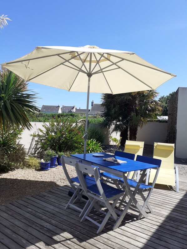 A wooden deck with a table and chairs under a large umbrella.