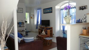 Una sala de estar con televisor, una mesa de madera y un sofá. Hay una ventana con cortinas y una planta en el alféizar.