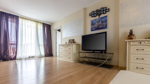 A spacious living room with a large flat-screen TV, a white cabinet, and a glass TV stand. - Two Bedroom Apartment, Terrace in Aphrodite Palace (Sunny Beach)
