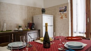 A kitchen with a dining table set for two, a refrigerator, and a calendar on the wall. - Casa Tonno (Alghero)