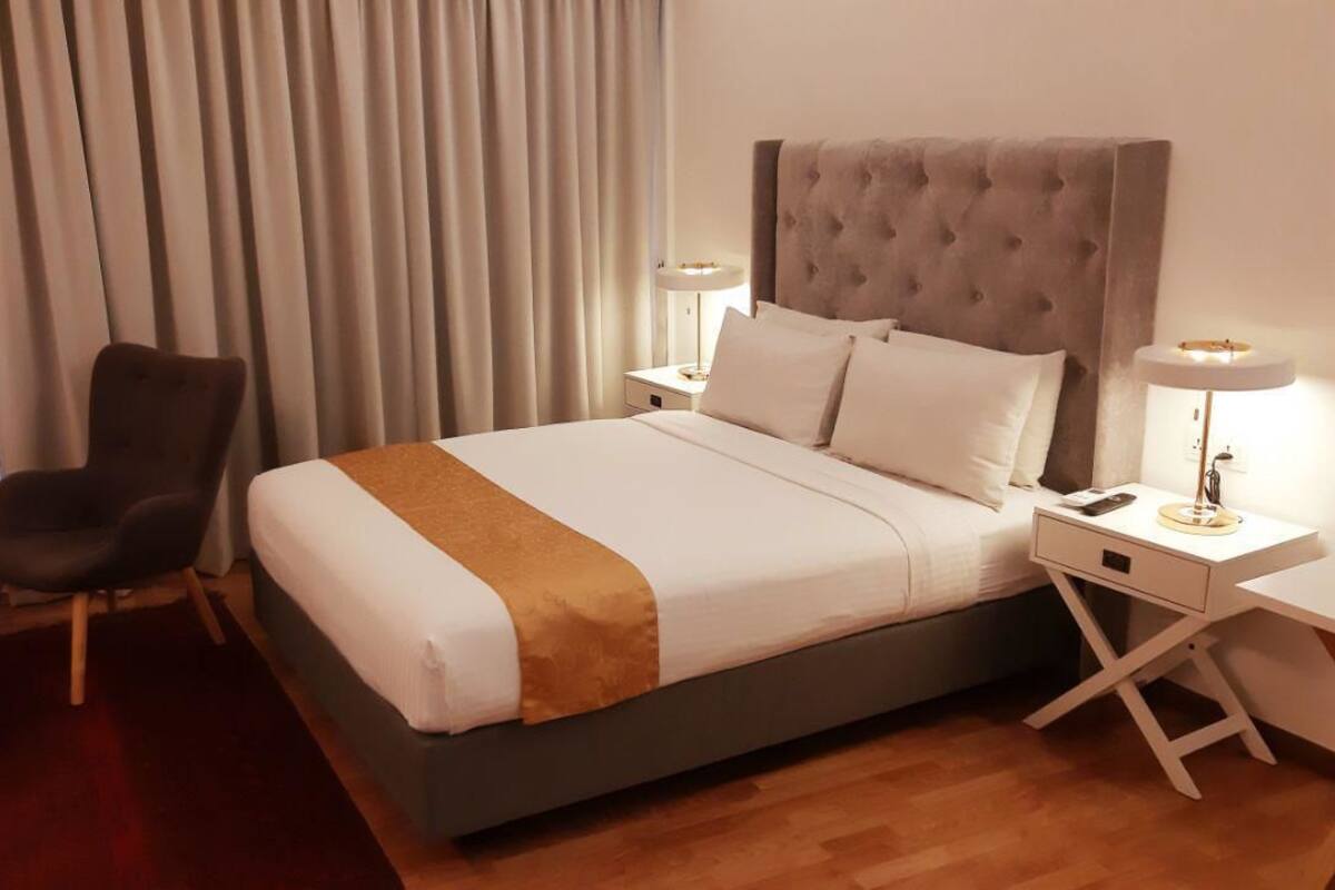A hotel room with a large bed, a chair, a nightstand, and a lamp.