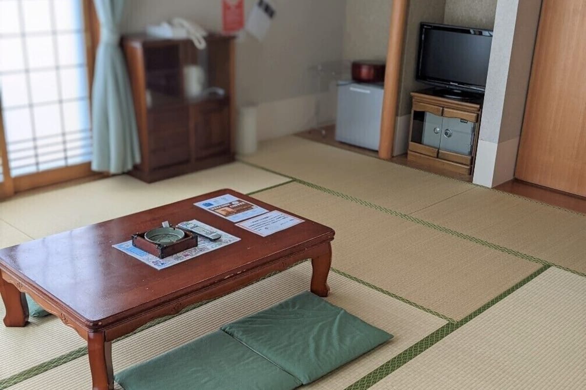 Une pièce de style japonais traditionnel, avec un sol recouvert de tatamis, une petite table en bois avec un coussin, un téléviseur et un meuble.