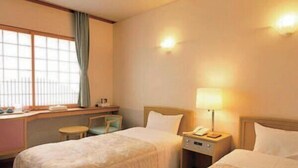A hotel room with two beds, a desk, a chair, a lamp, and a window with curtains.