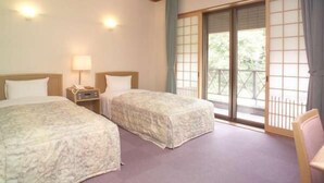 A hotel room with two beds, a nightstand, a lamp, and a sliding glass door to a balcony.