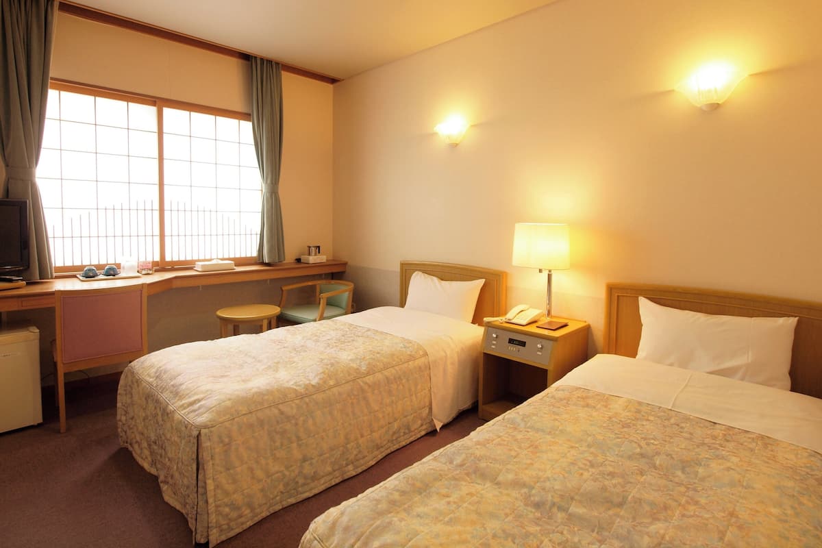 Une chambre d’hôtel avec deux lits, un bureau, une chaise, une télévision et une fenêtre avec des rideaux.