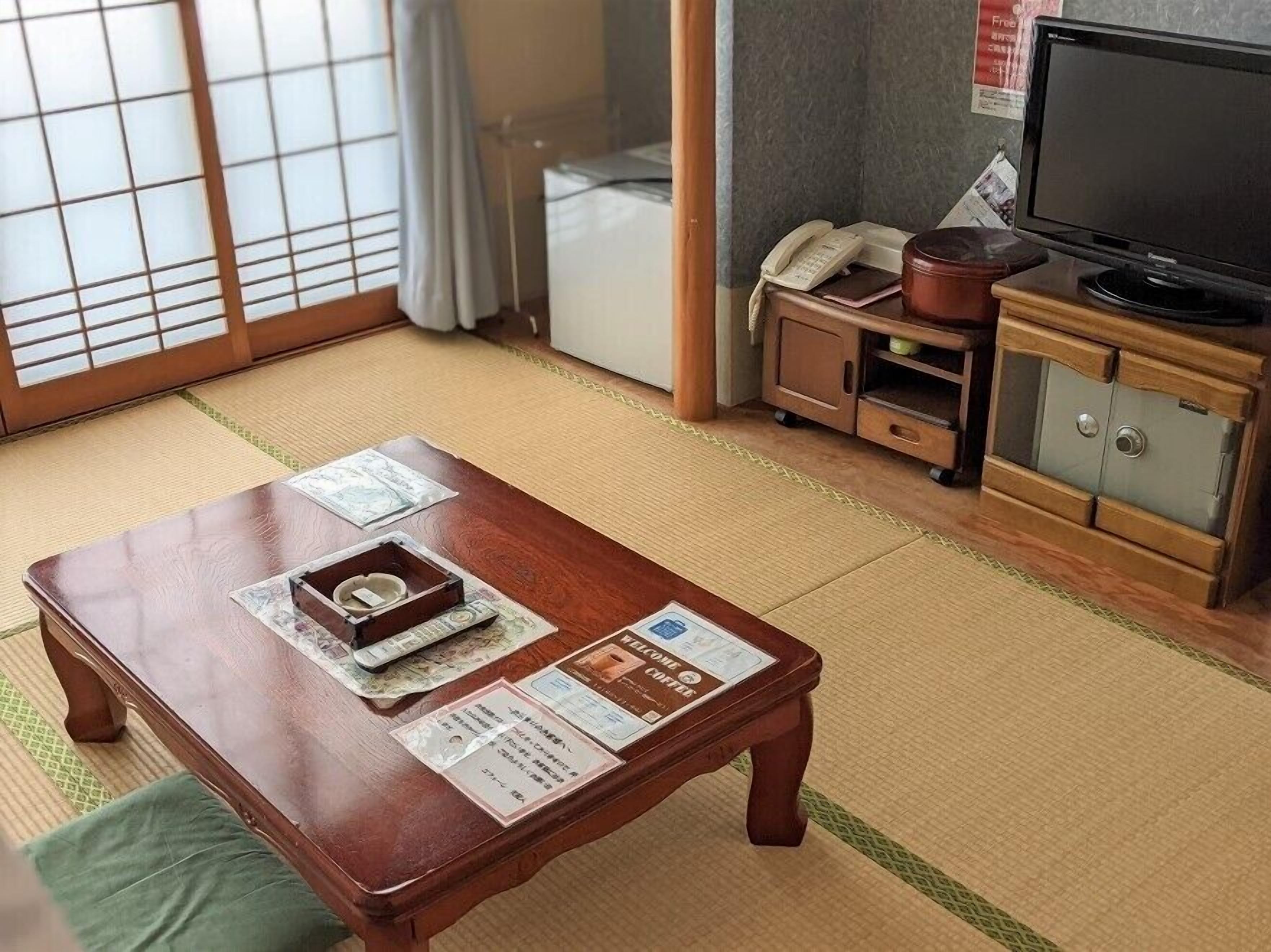 Een traditionele Japanse kamer met tatami vloerbedekking, een houten tafel met dienblad, een televisie en een kast met een kluis.