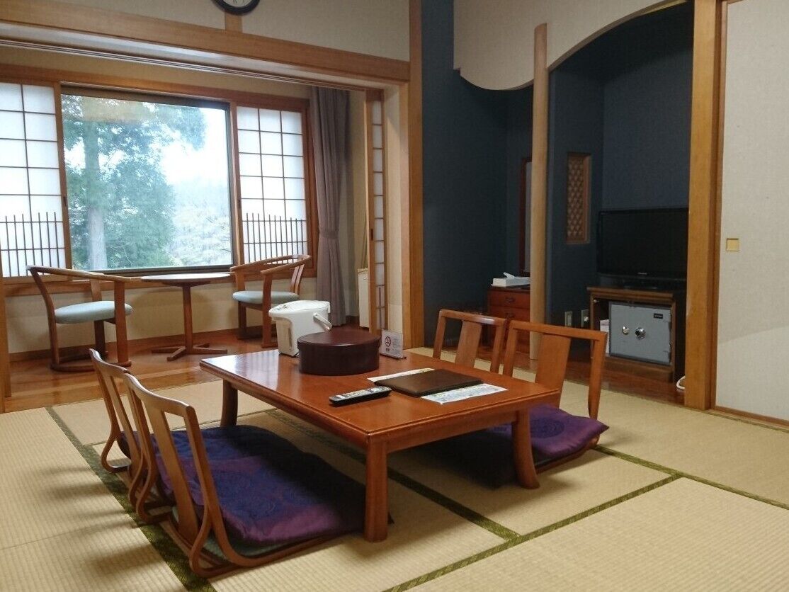 Een traditionele Japanse kamer met tatami vloerbedekking, een lage tafel met kussens, een televisietoestel en een kluis.