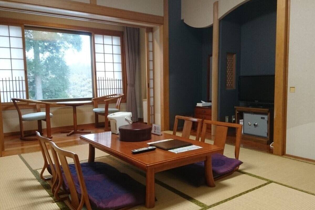 Une pièce de style japonais traditionnel, avec un sol recouvert de tatamis, une table basse avec des coussins, un téléviseur et un coffre-fort.
