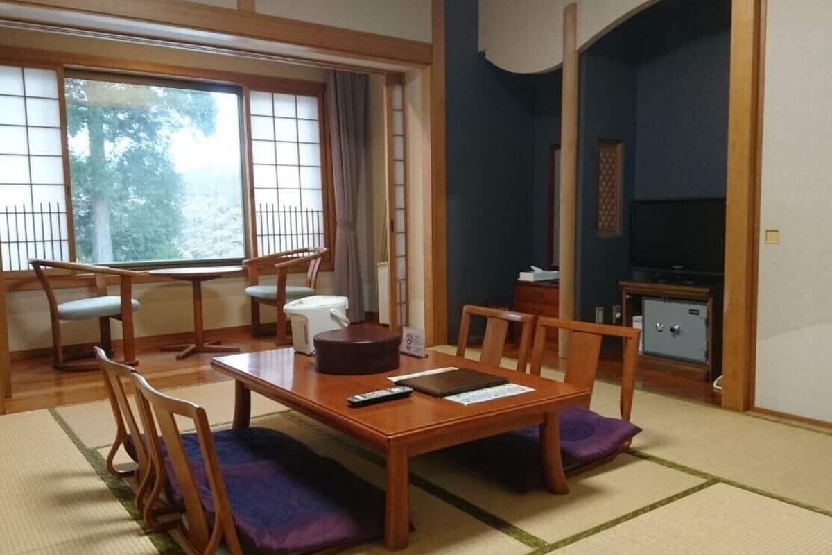 A traditional Japanese room with tatami flooring, a low table with cushions, a television, and a safe.
