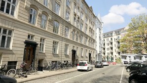 A street with parked cars and bicycles, a building with multiple windows and balconies, and a clear sky. - 2 bedroom apartment Vesterbro 1372-1 (Copenhagen)