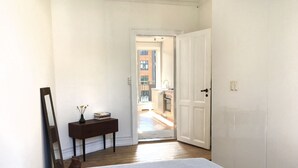 A narrow hallway with a bed, a dresser, and a mirror. A door leads to a kitchen area. - 2 bedroom apartment Vesterbro 1372-1 (Copenhagen)