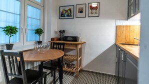 A compact kitchen with a wooden table, two chairs, a small shelf, and a window with potted plants. - Boutique Prater Apartment Vienna (Vienna)