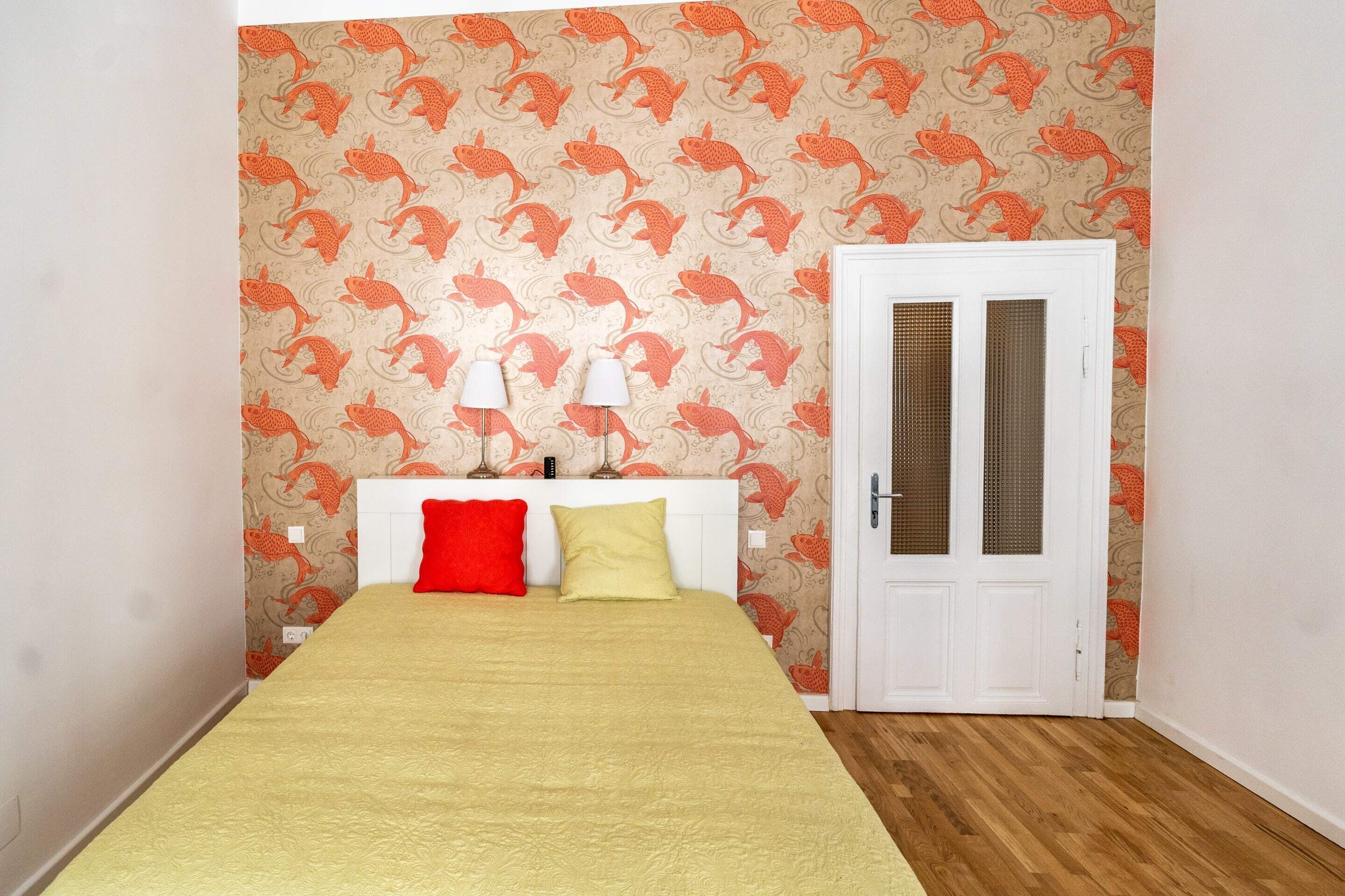 A bedroom with a bed, two bedside lamps, a white door, and a patterned wallpaper.