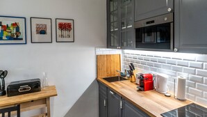 A modern kitchen with dark cabinets, a wooden countertop, and a white brick backsplash. There are framed artworks on the wall and a coffee machine on the counter. - Boutique Prater Apartment Vienna (Vienna)