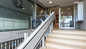 A staircase with a handrail, leading to an interior space with a glass wall displaying a logo and text.