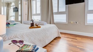 A hotel room with a large bed, a flat-screen TV mounted on the wall, and a view of the sea through the windows. - Luxury White Villa Sea View, Pool (Adeje)