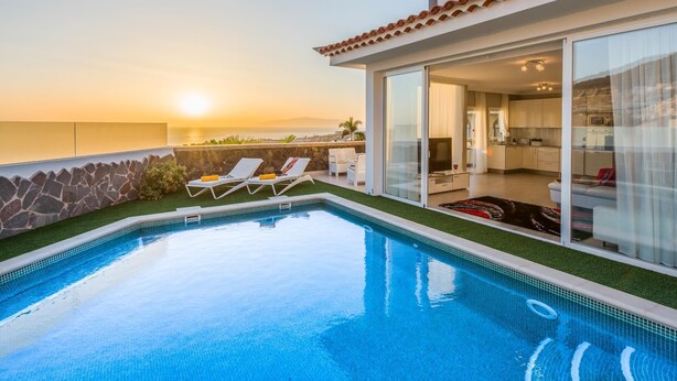 A modern pool area with a clear view of the sunset over the ocean, a stone wall, and two lounge chairs. - Luxury White Villa Sea View, Pool (Adeje)